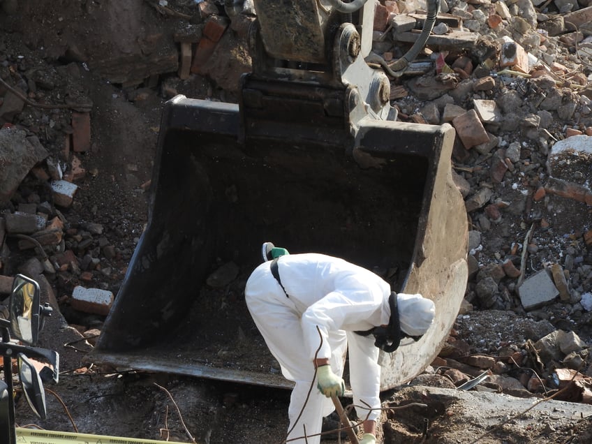 Demolition costs- Worker with white protective suit, gloves and mask removes removal white asbestos on construction site. Demolition building with excavator. Action picture, part of a serie.